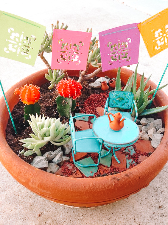 mini garden with colourful Mexican banner, teal patio set, cacti, aloe, rocks and pottery